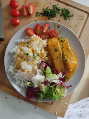 talerz, a na nim łośoś w curry, ryż jaśminowy, sałata i pomidory