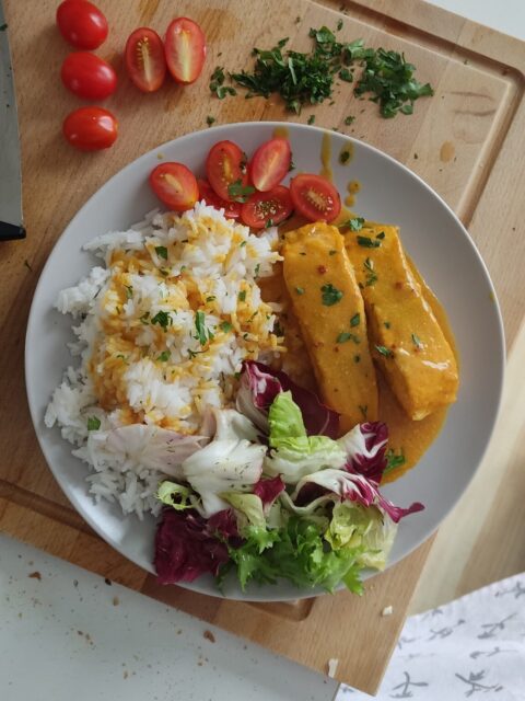 talerz, a na nim łośoś w curry, ryż jaśminowy, sałata i pomidory