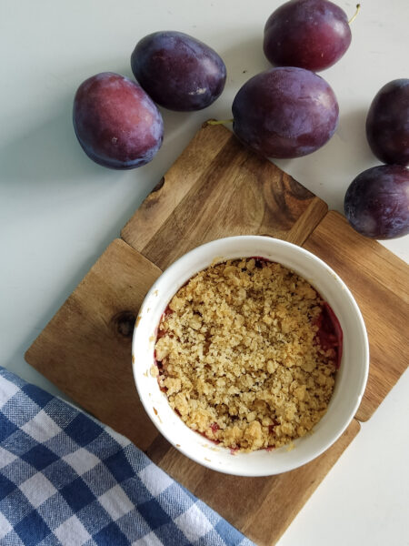 Crumble ze śliwkami w kokilce, obok świeże śliwki